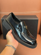 Prada unisex leather loafer close-up, dark glossy upper with buckle detail, chunky sole