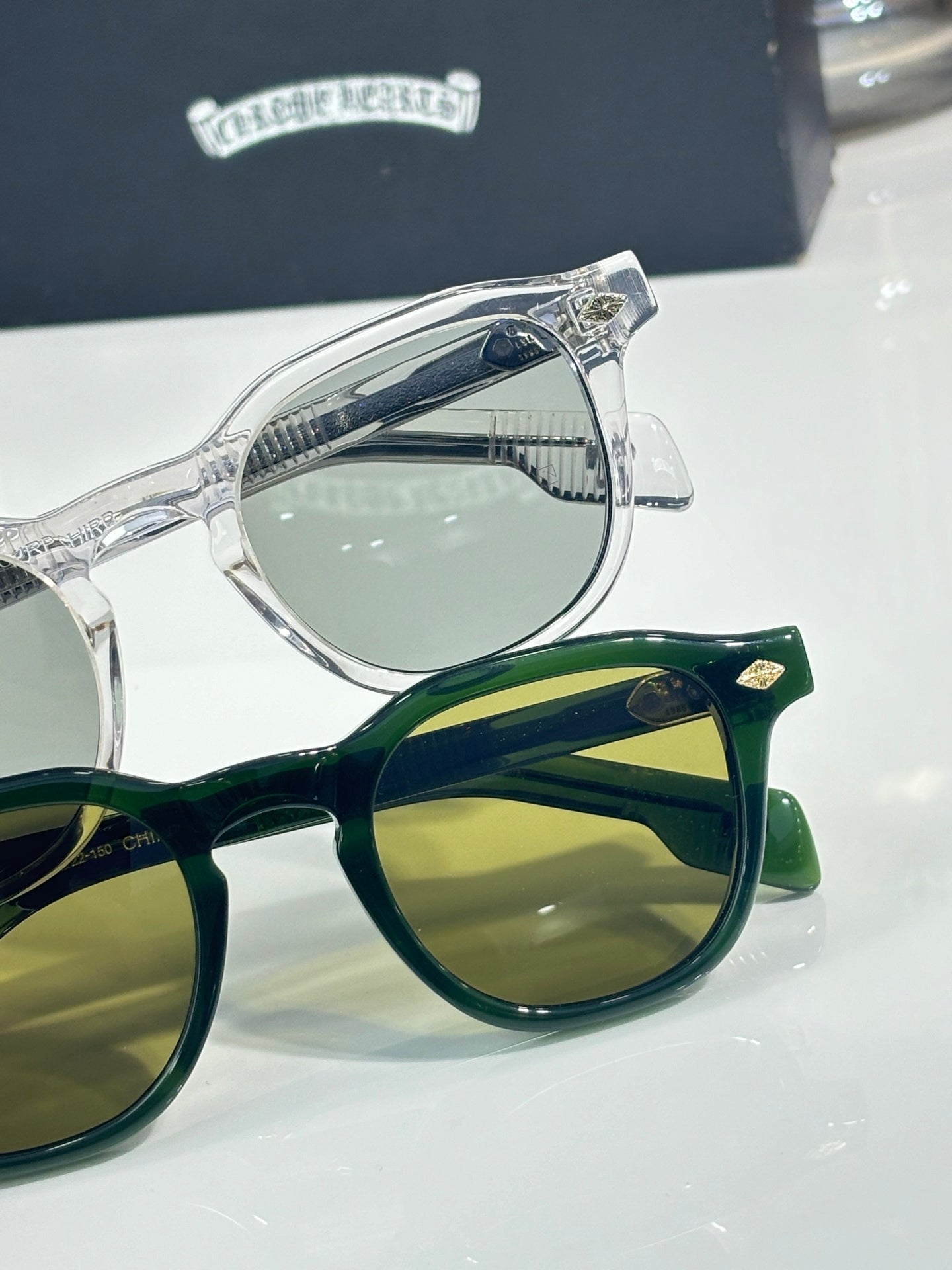 Clear chrome and green sunglasses close-up, with patterned temple details.
