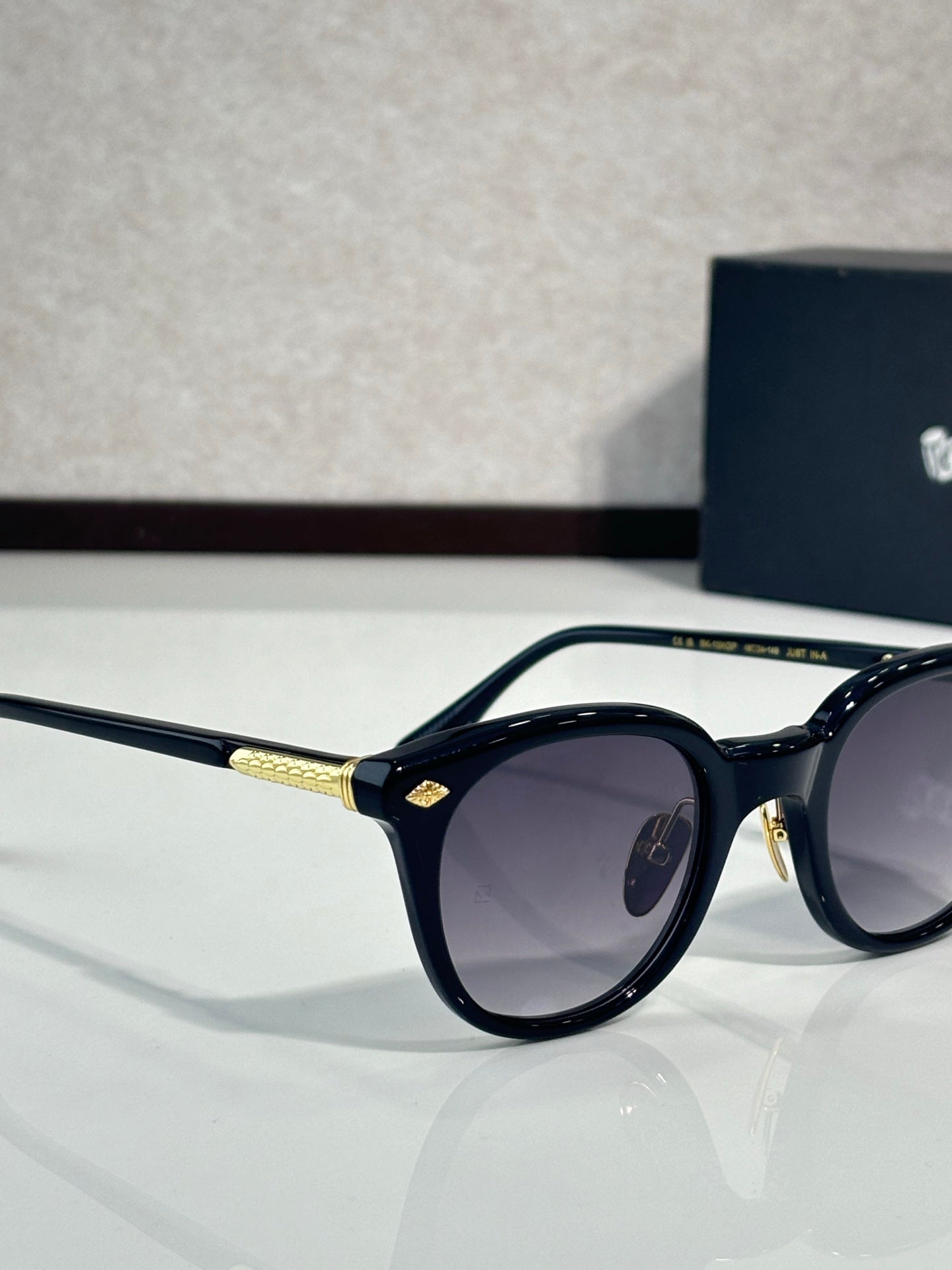 Black oval eyeglasses with dark purple lenses and gold-tone bridge