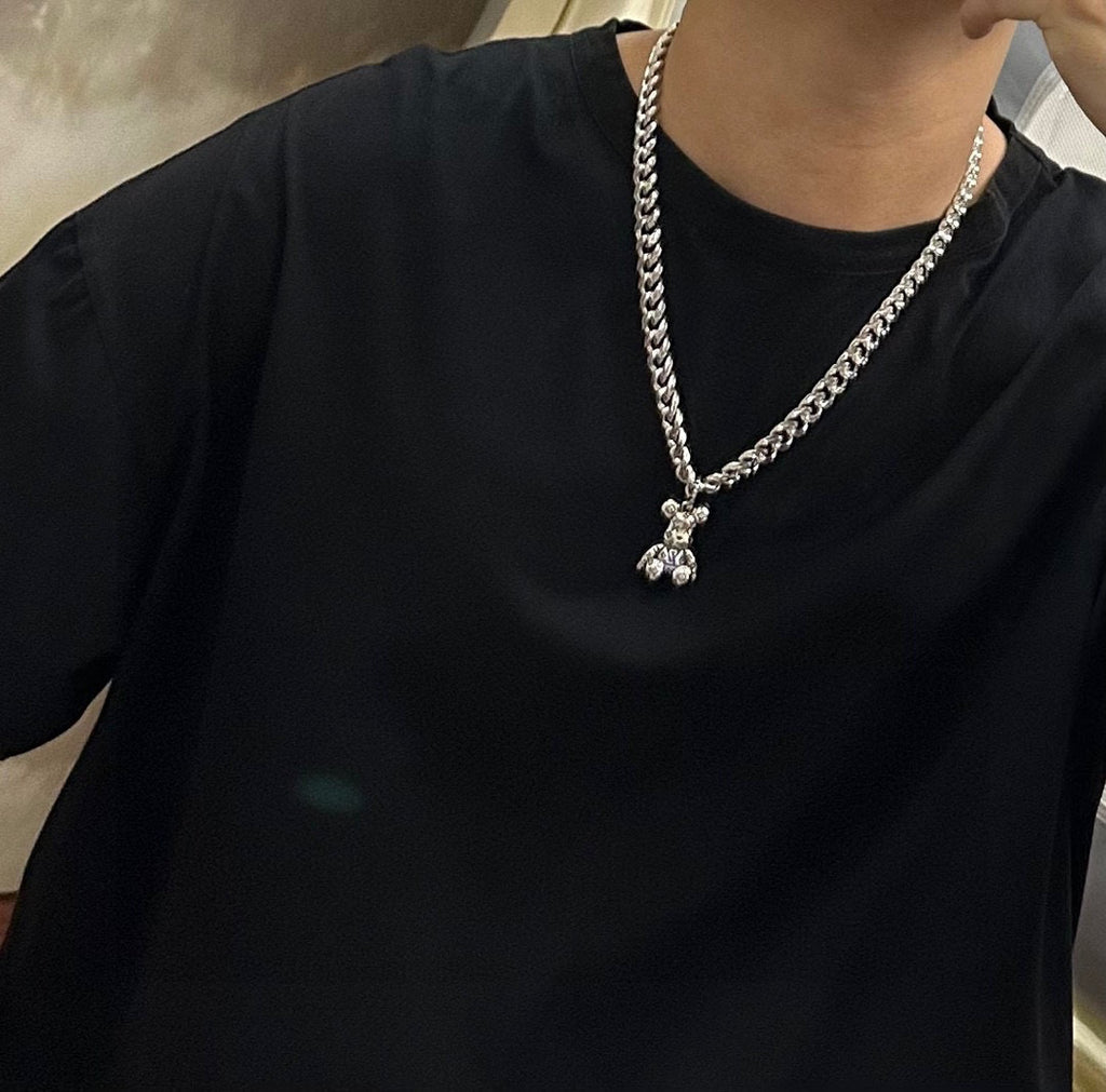 Silver chain necklace with small flower-like charm pendant, worn on dark shirt
