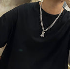 Silver chain necklace with small flower-like charm pendant, worn on dark shirt