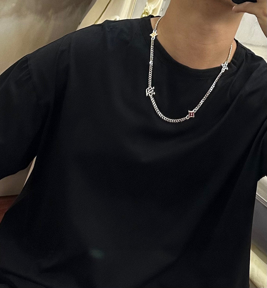 Silver-tone charm necklace worn over black crewneck top, featuring star charms