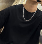 Silver-tone charm necklace worn over black crewneck top with small hanging charms