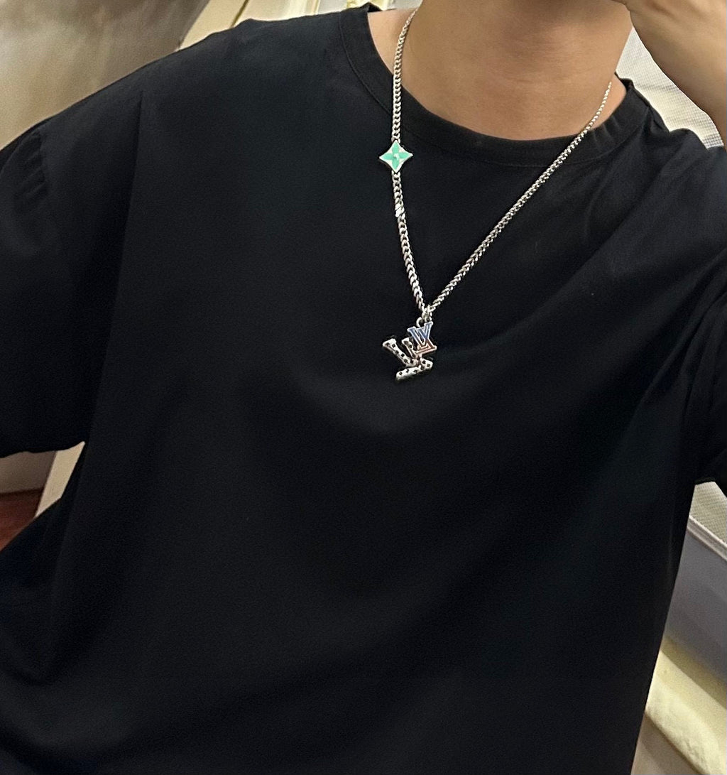 Silver-tone chain necklace with green star charm and small pendant on black T-shirt