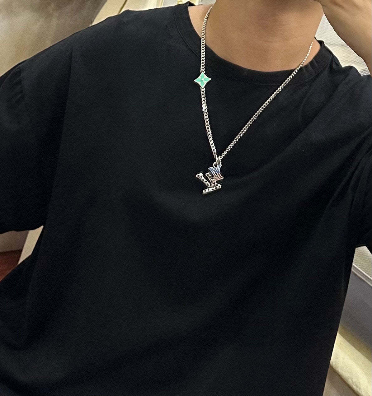 Silver-tone chain necklace with green star charm and small pendant on black T-shirt