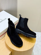 Black suede Chelsea boots on round pedestal, elastic side panels and tread sole.