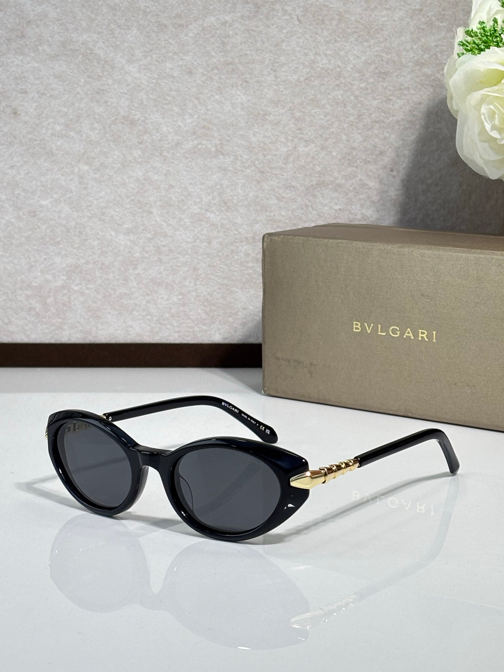 Black oval sunglasses with dark tinted lenses and gold logo temple arms