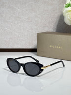 Black oval sunglasses with dark tinted lenses and gold logo temple arms
