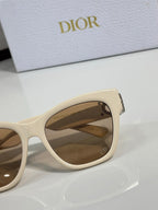 Cream cat-eye sunglasses close-up with gold logo charm and tinted lens