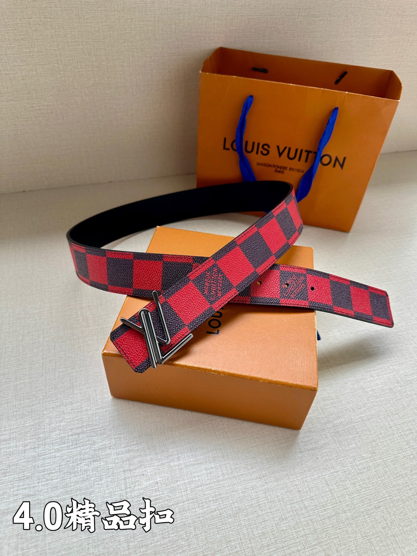 Checked belt layered on boxes; red-and-navy pattern with metal V buckle