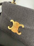 Gray Celine handbag close-up of gold emblem on front flap.