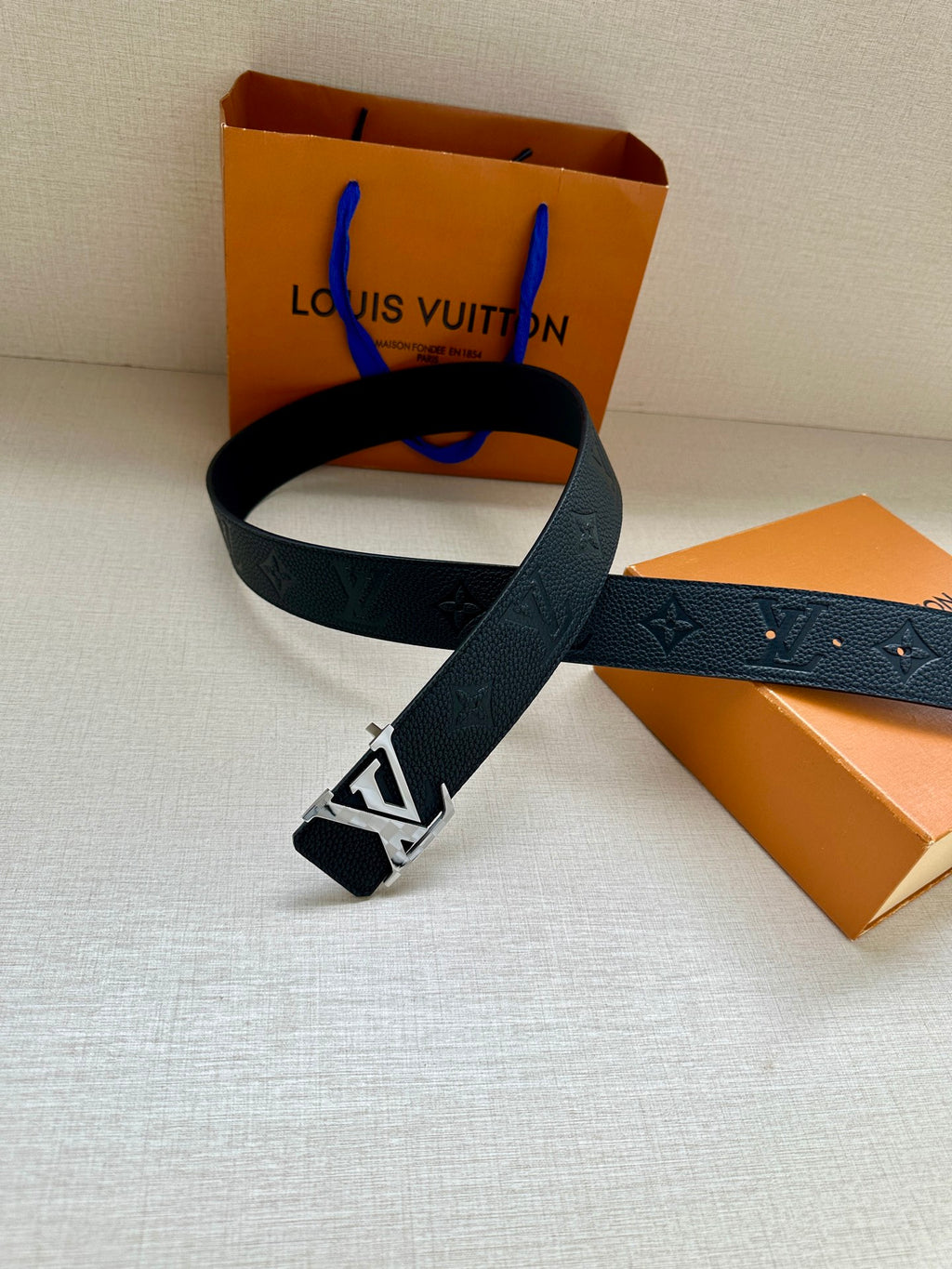 Louis Vuitton belt with dark blue strap and silver LV buckle, shown looped