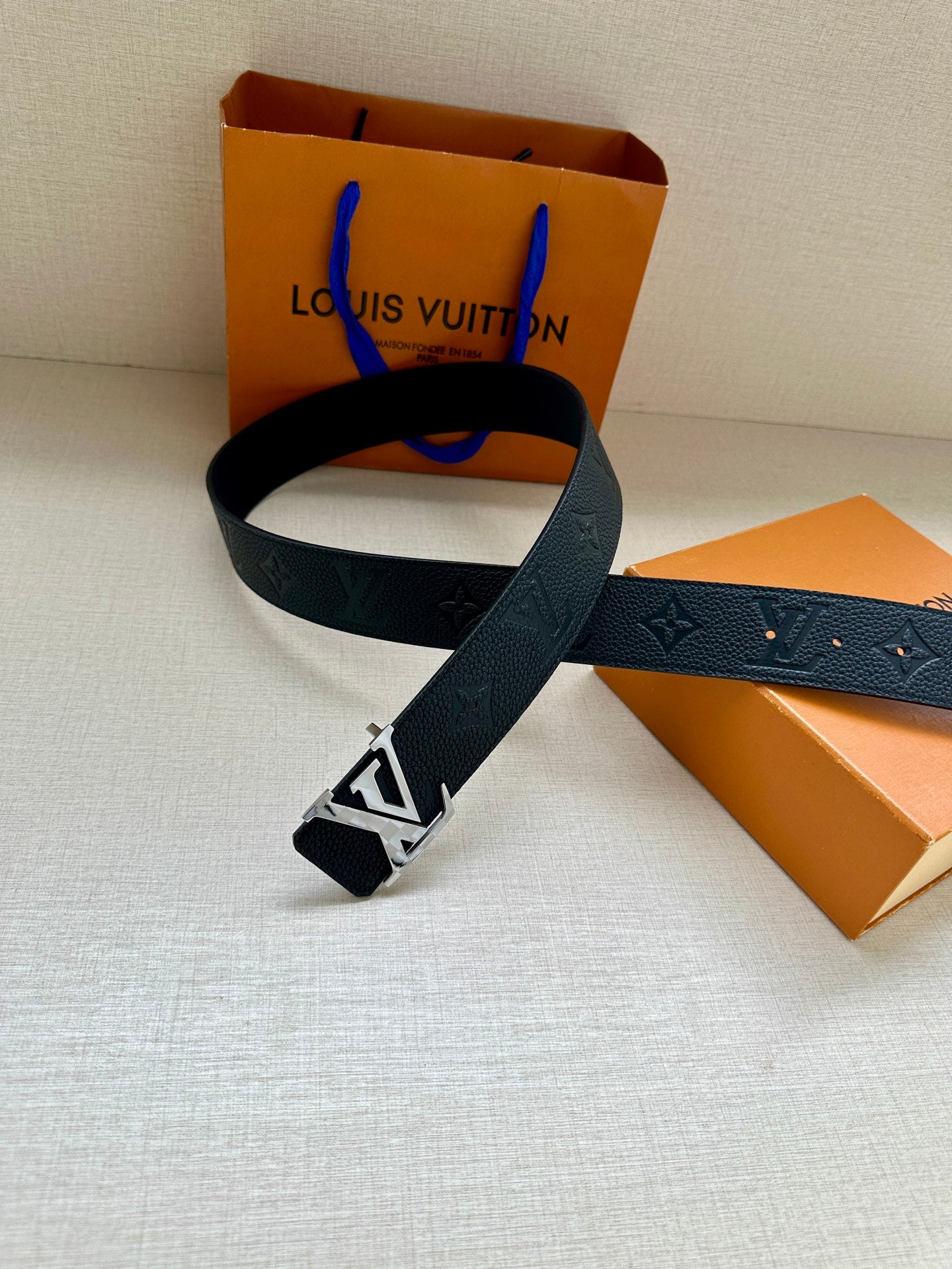 Louis Vuitton belt with dark blue strap and silver LV buckle, shown looped