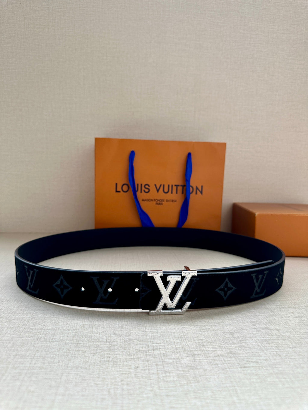 Monogram canvas belt with dark blue strap and silver-tone buckle, flat on surface