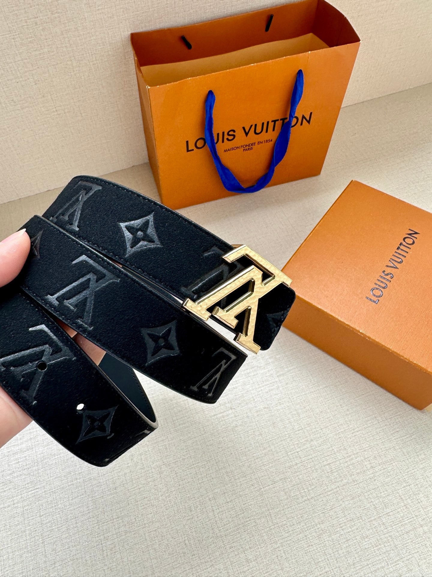 Monogram canvas belt close-up with metal buckle detail and dark blue strap