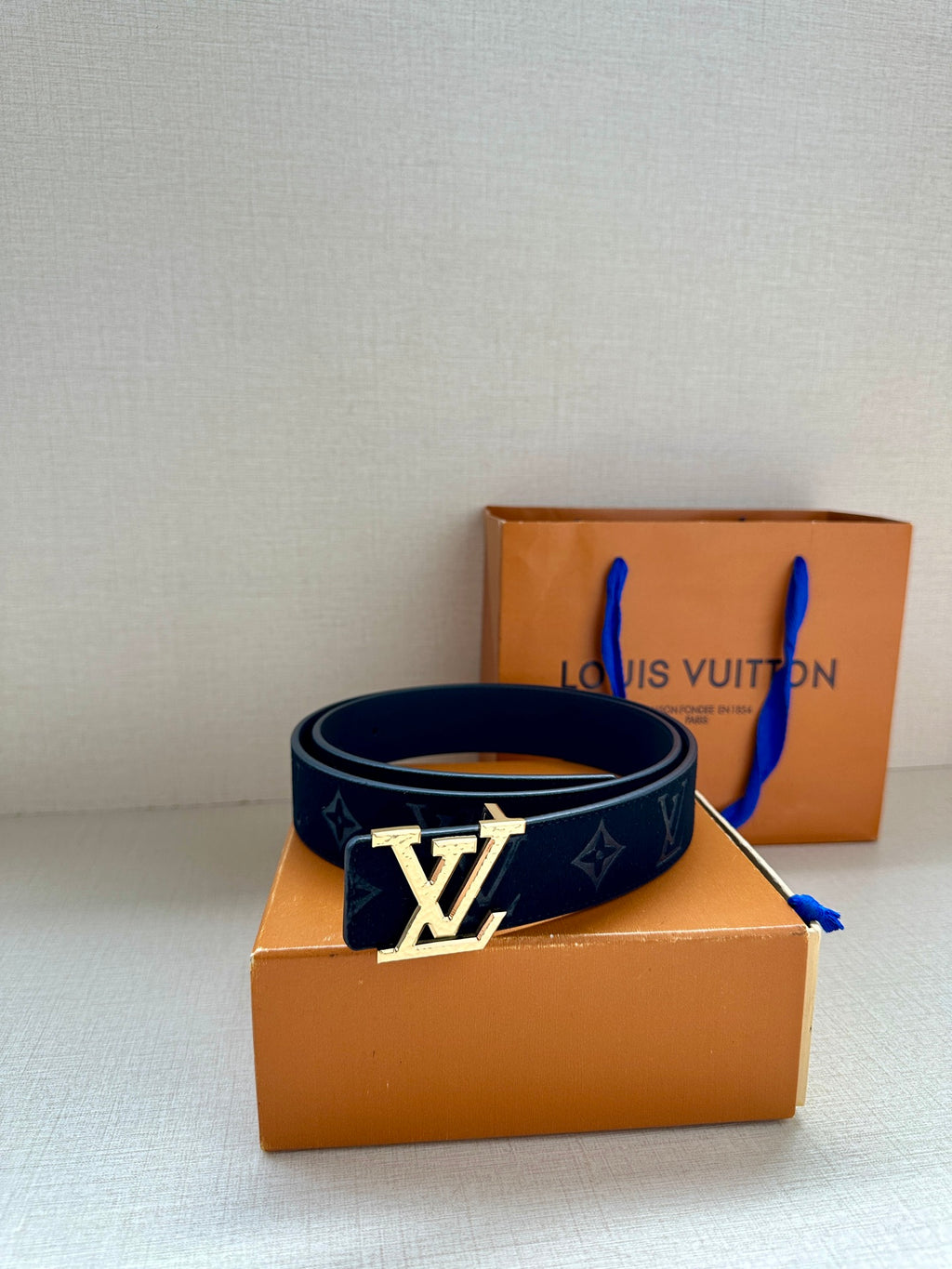 Monogram belt with dark blue strap and silver-tone buckle, resting on surface