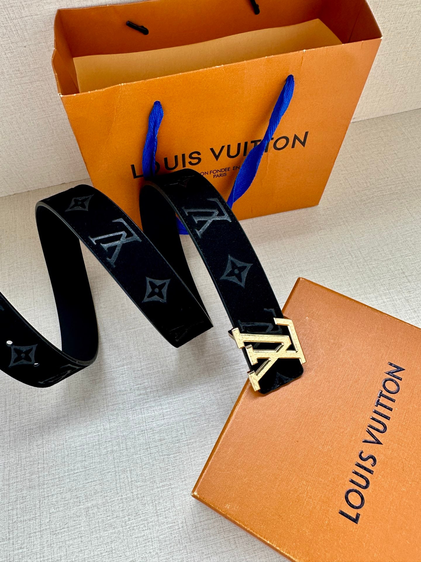 Monogram belt with long dark blue strap ends and silver-tone buckle, angled view