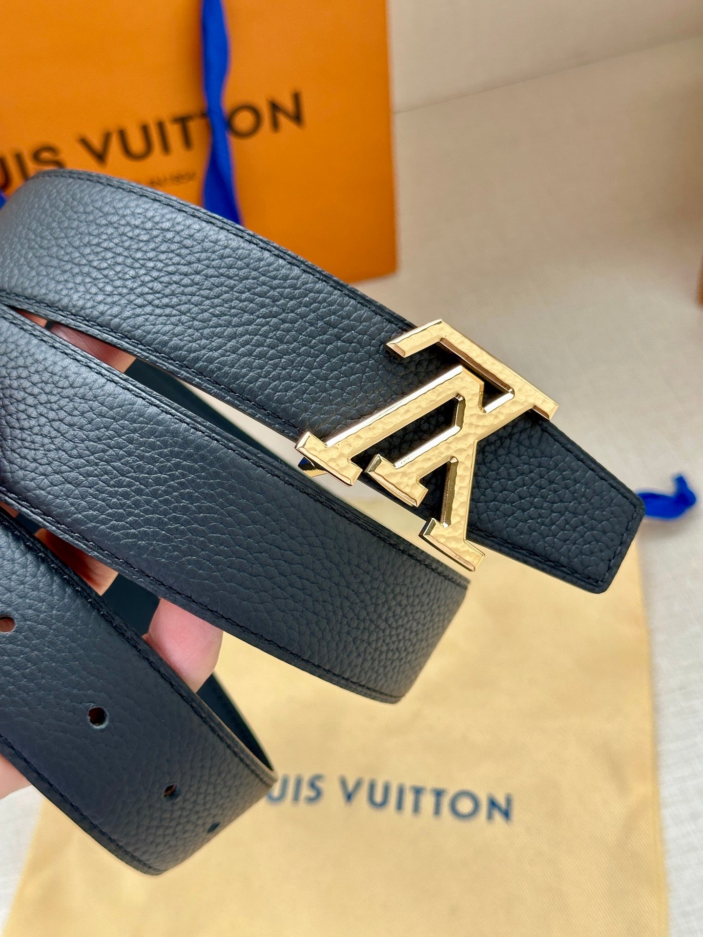Dark blue leather belt with large gold LV buckle, belt tail and strap holes visible.