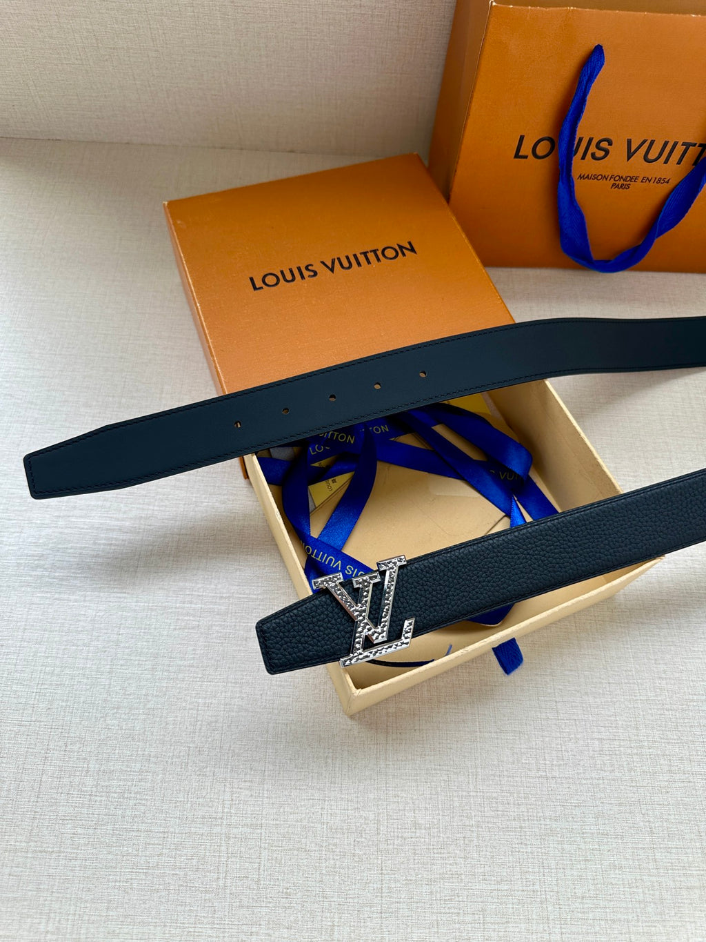 Dark blue leather belt with gold LV buckle, shown laid diagonally over box.