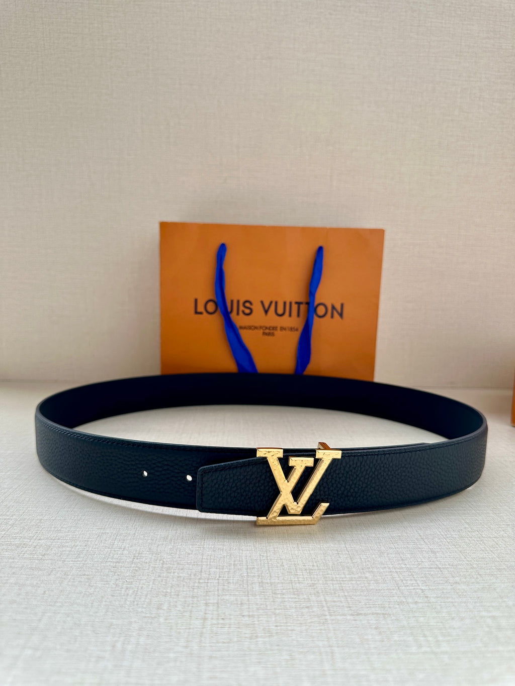 Dark blue leather belt with gold LV buckle centered on the strap.