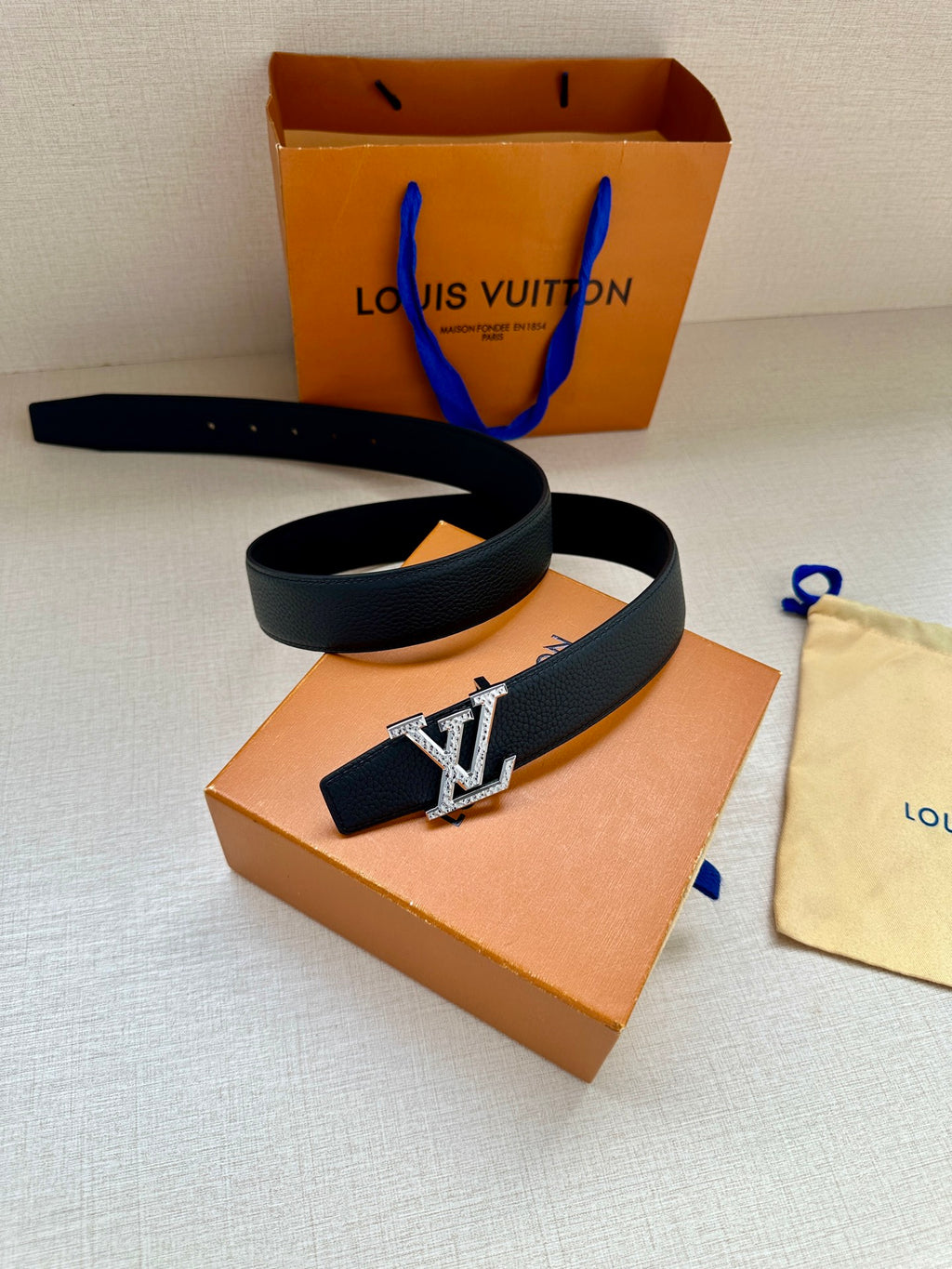 Dark blue leather belt with gold LV buckle, coiled with box and dust bag nearby.