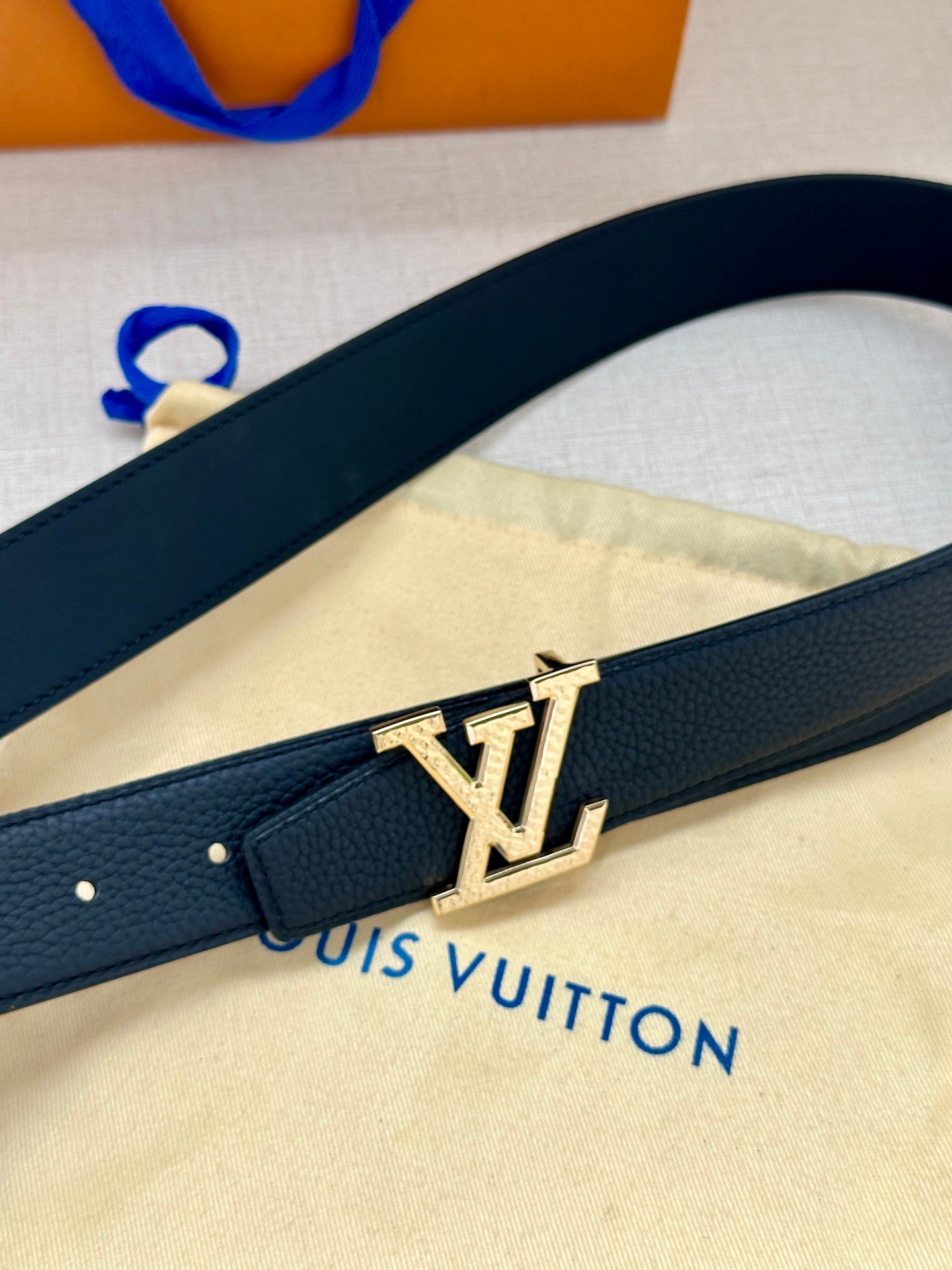 Dark blue leather belt with gold LV buckle, shown from side angle on strap.