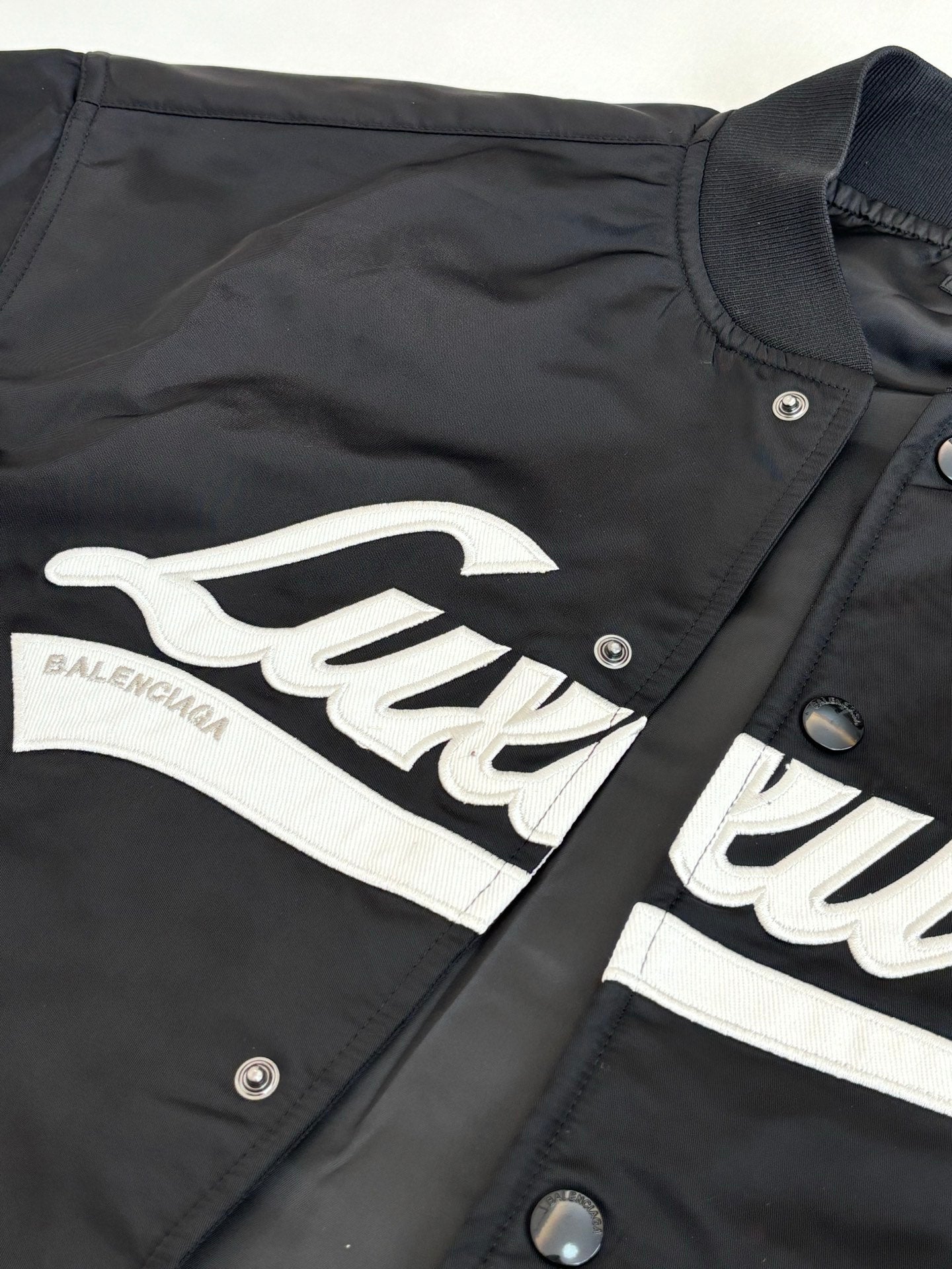 Dark bomber jacket with white logo graphic across chest and snap buttons