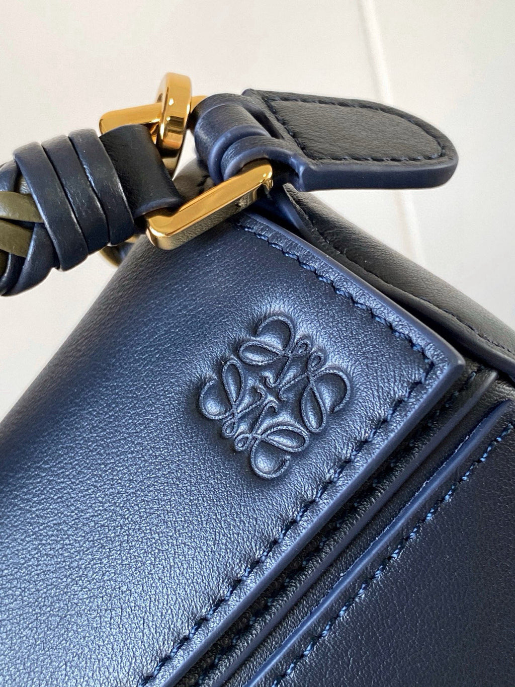 Blue leather bag corner with embossed floral logo and decorative stitching