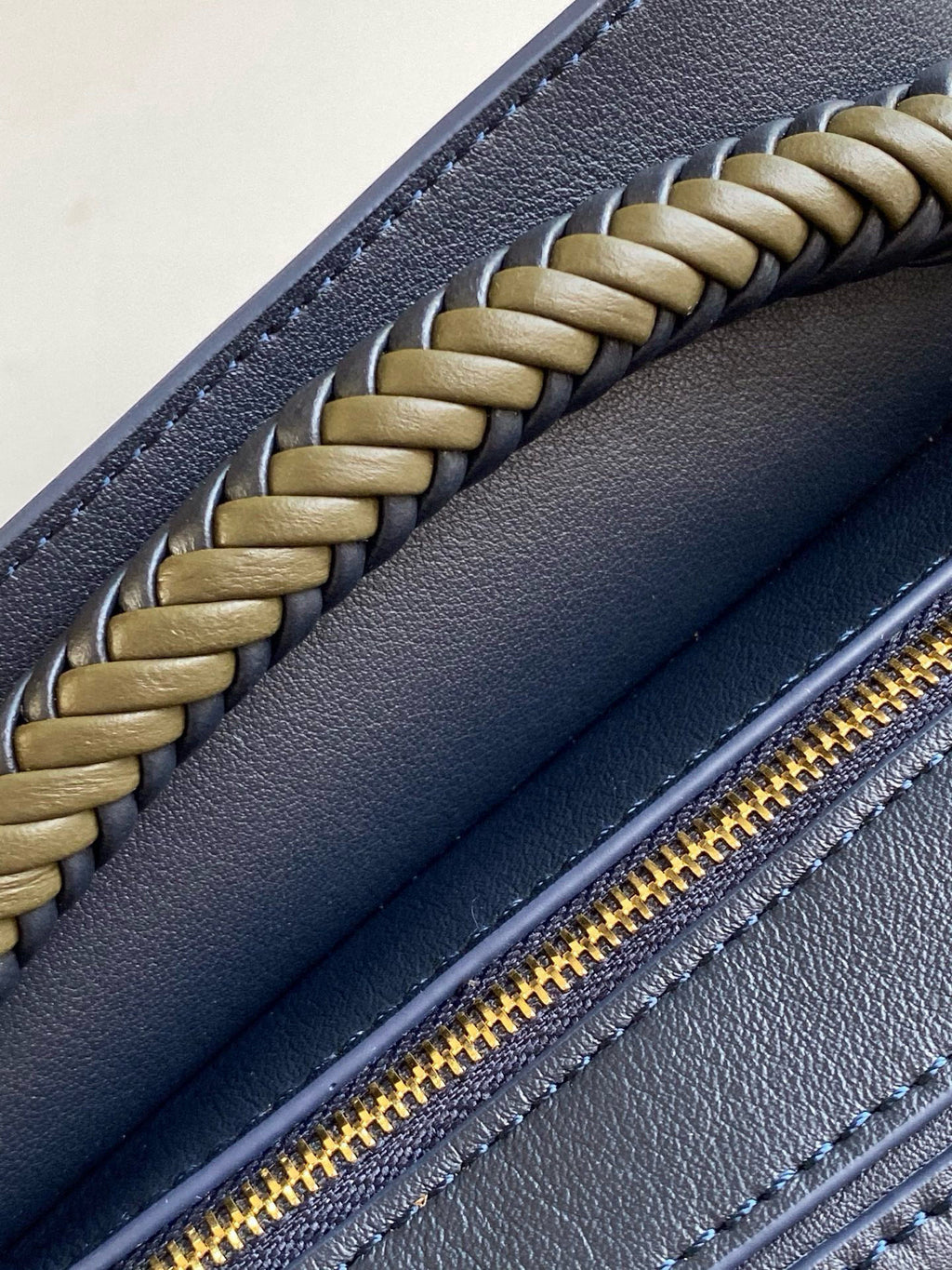 Blue leather bag detail: braided strap and gold zipper along top edge