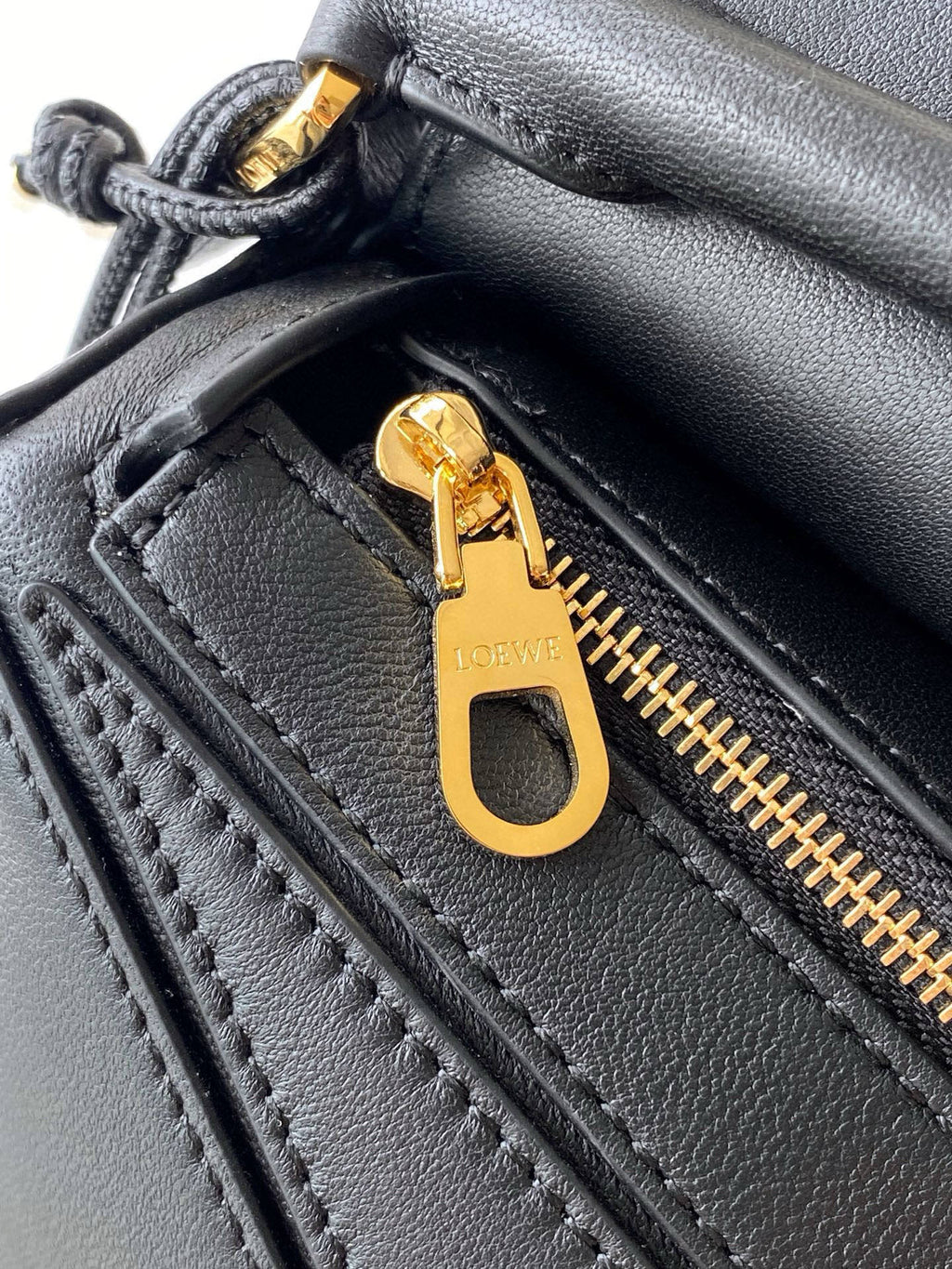 Loewe men’s black leather bag close-up with gold zipper pull and stitched panel details.