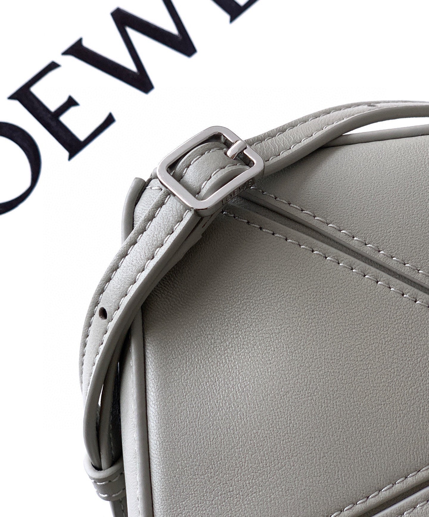 Gray leather bag corner with strap attachment and visible stitching details