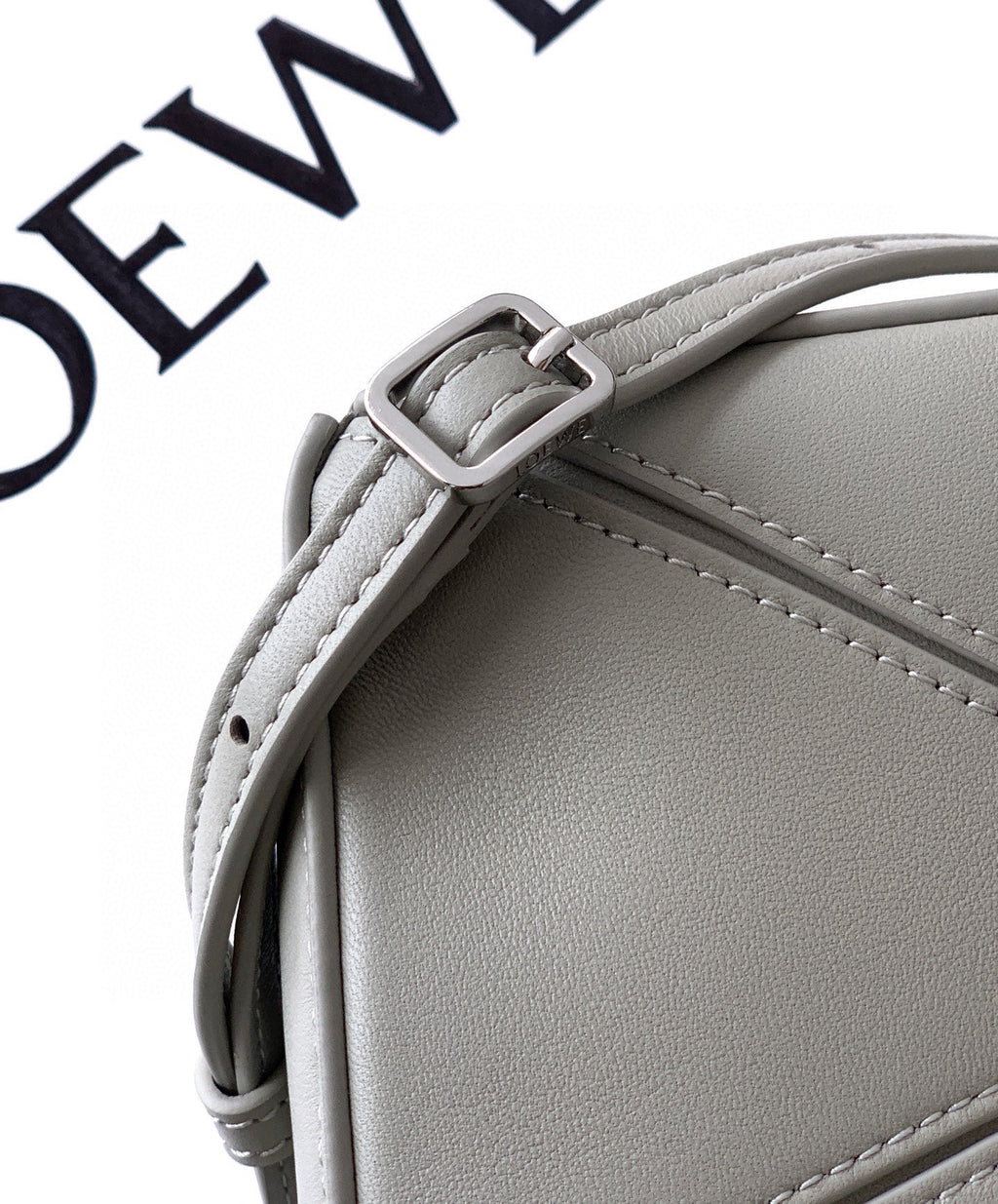 Light gray Loewe leather bag close-up of top edge, strap stitching, and buckle