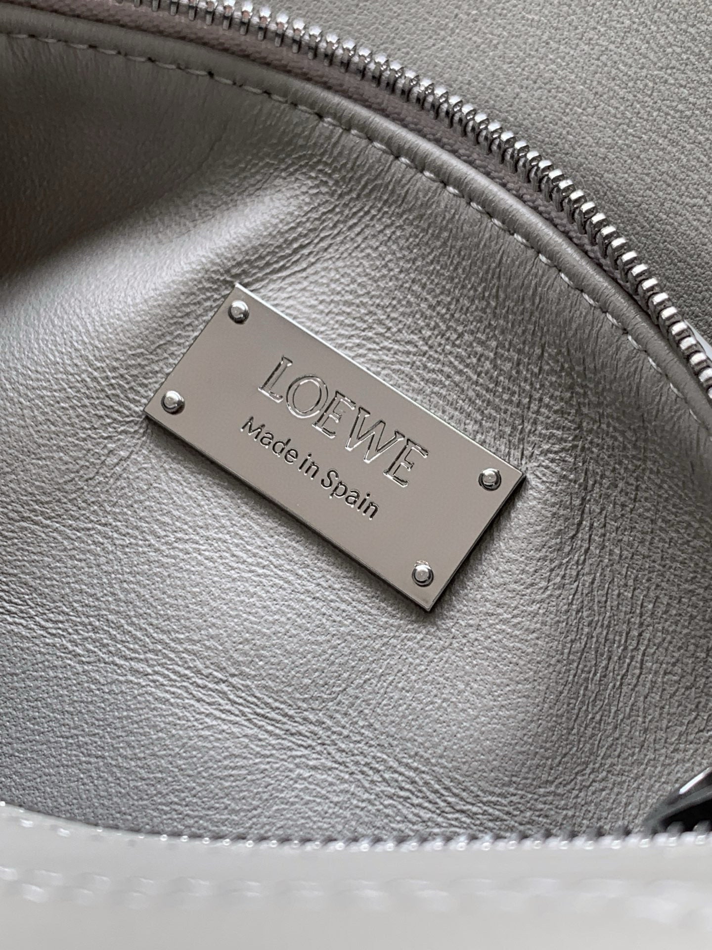 Light gray Loewe leather bag close-up of metal logo plate and zip track