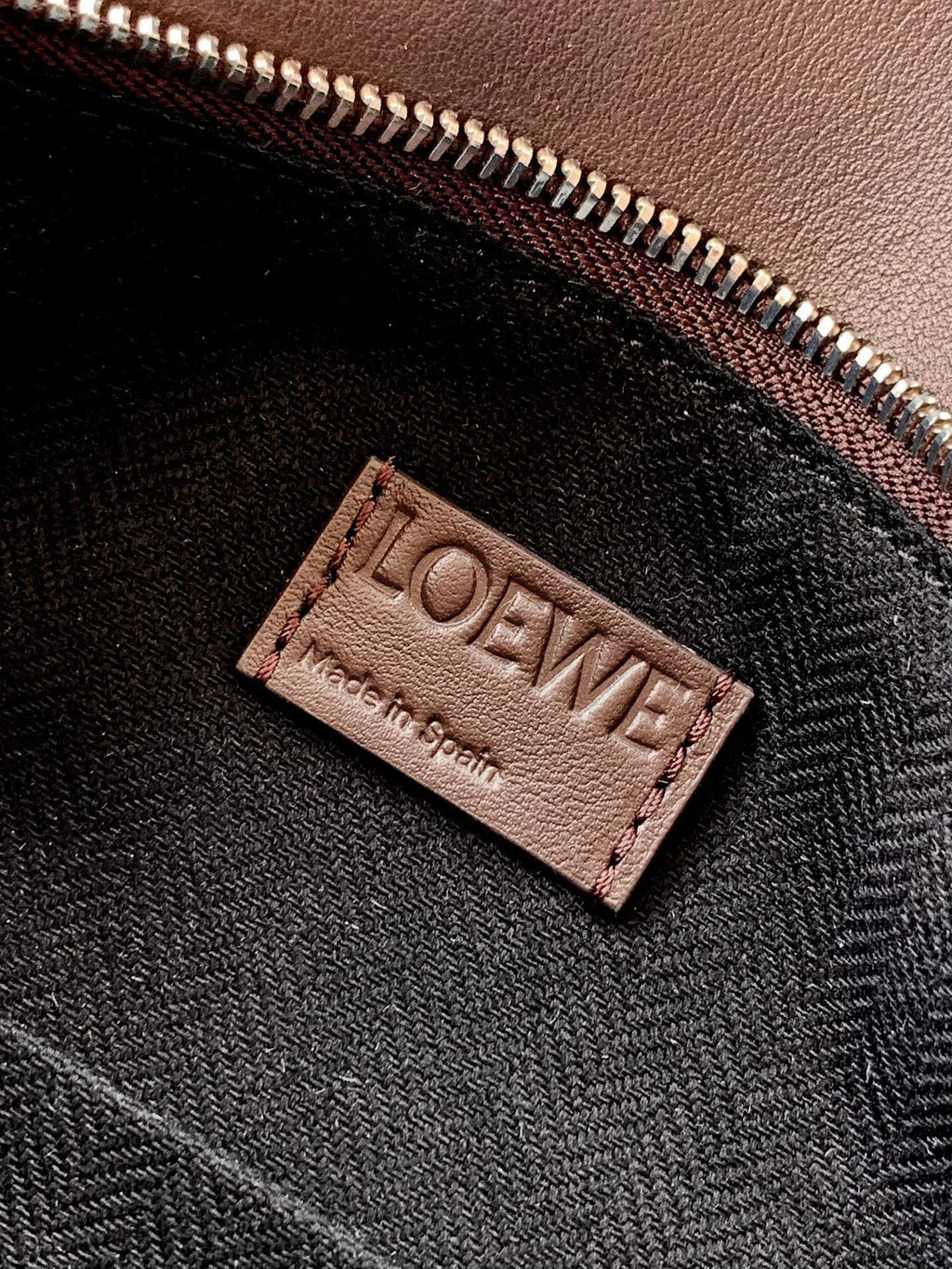 Leather bag lining label with LOEWE branding near zipper, dark taupe