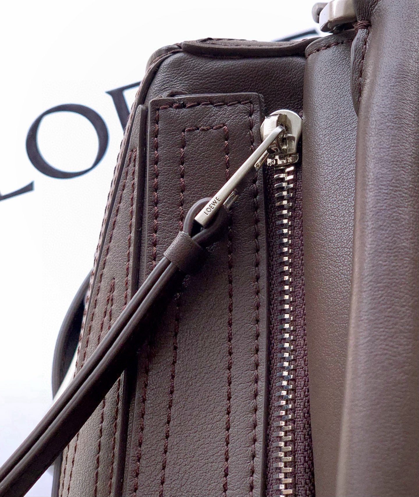 Leather bag side detail with zip pocket, silver zipper pull, and stitched panel, taupe