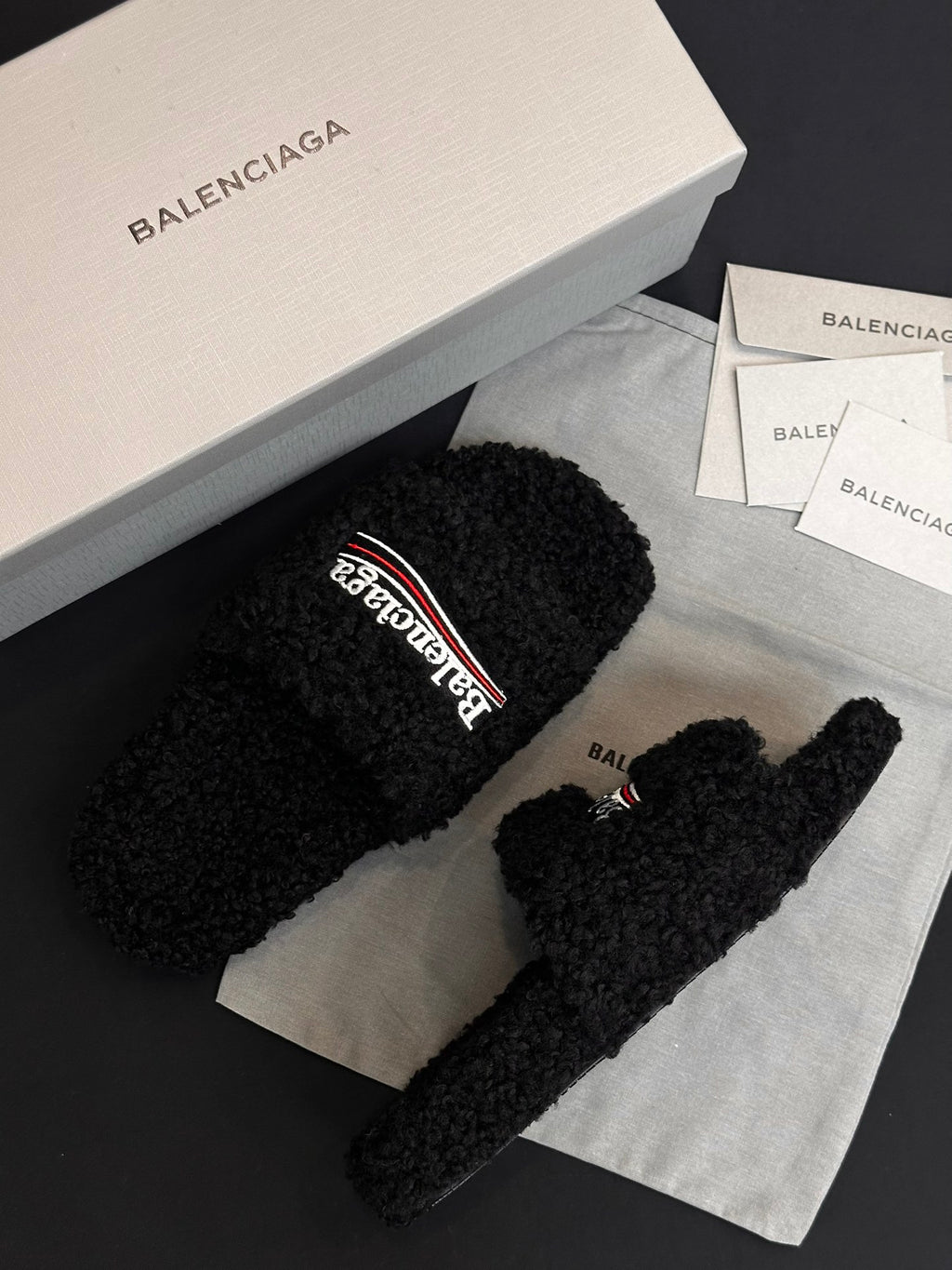 Black fuzzy slide sandals with Balenciaga logo strap, angled view