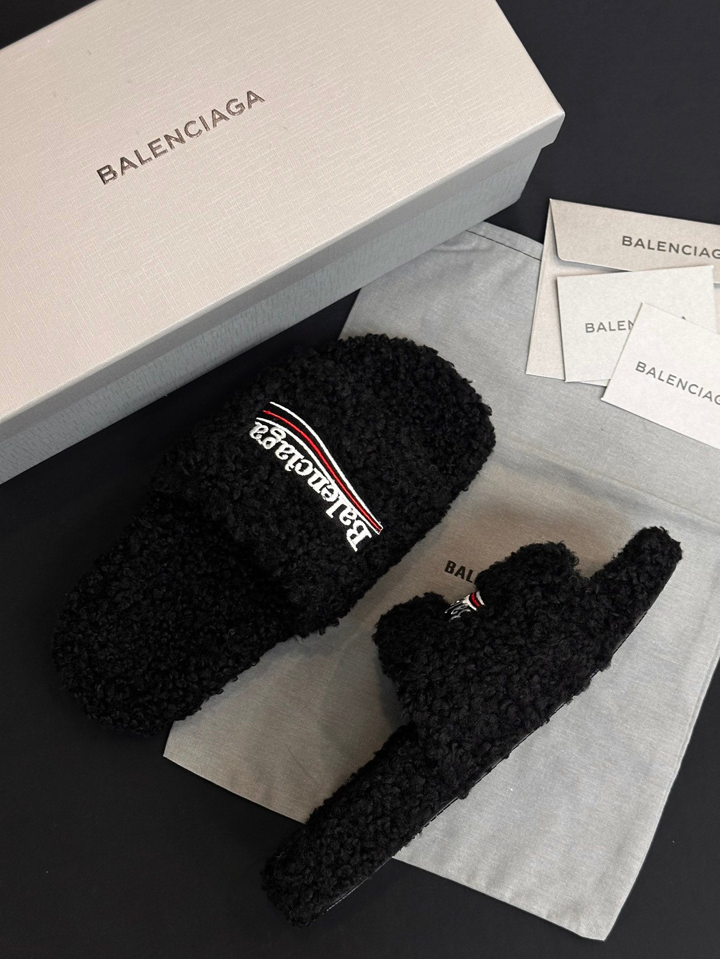 Black fuzzy slide sandals with Balenciaga logo strap, angled view