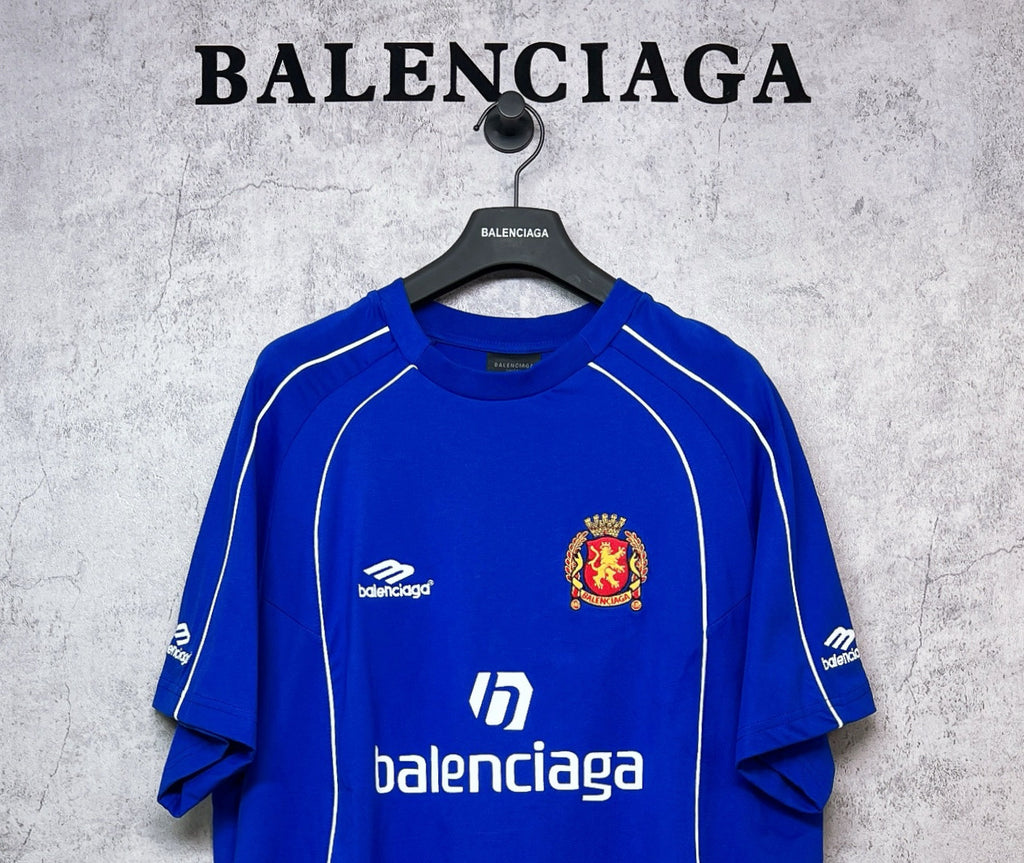 Blue short-sleeve jersey with white lines, small logo, and crest emblem