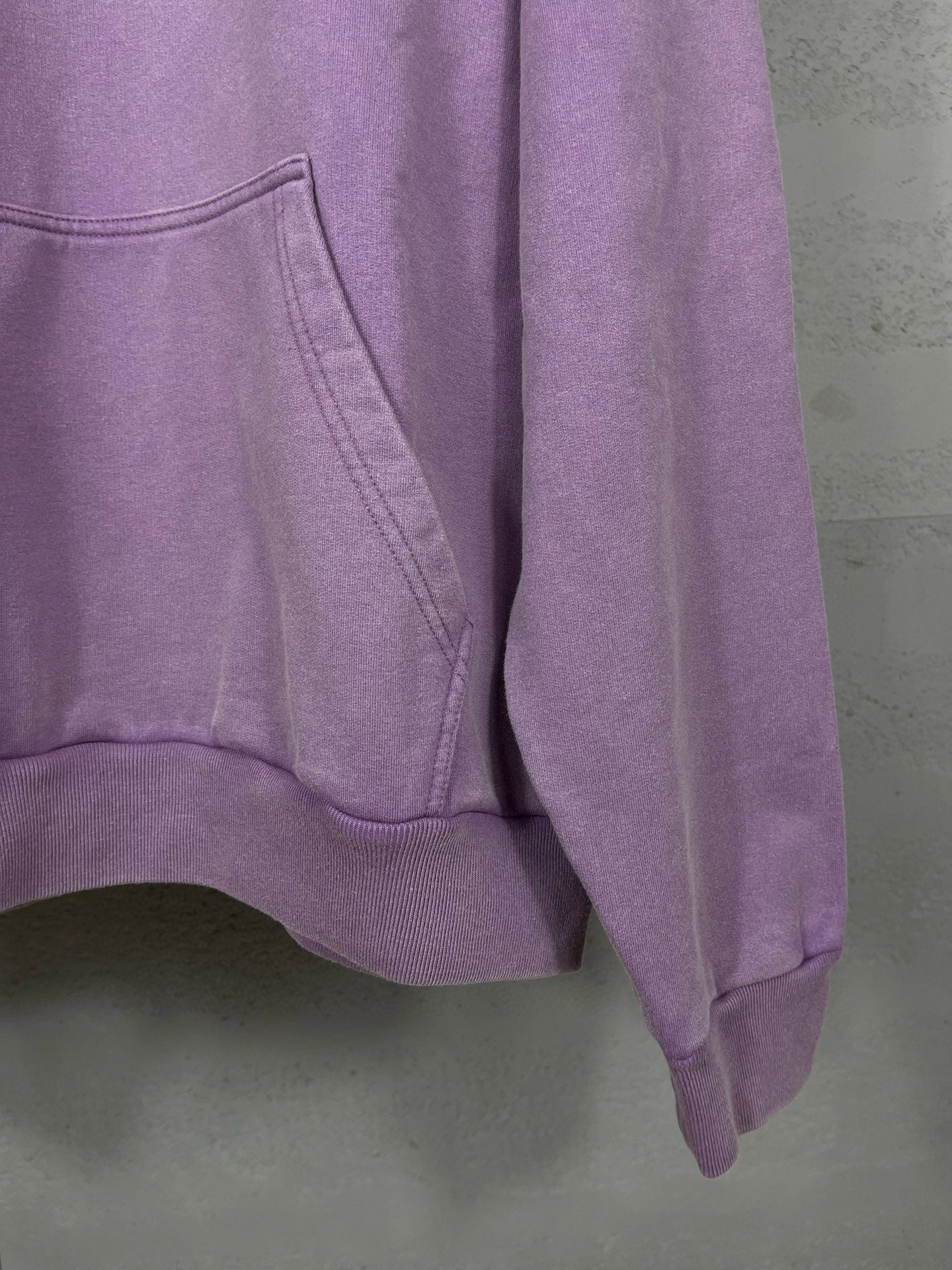 Purple long hoodie showing sleeve and kangaroo pocket seams at lower hem.