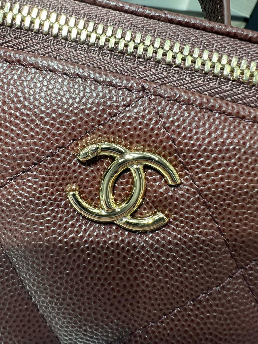 Maroon leather bag hardware with gold CC logo and zipper trim close-up