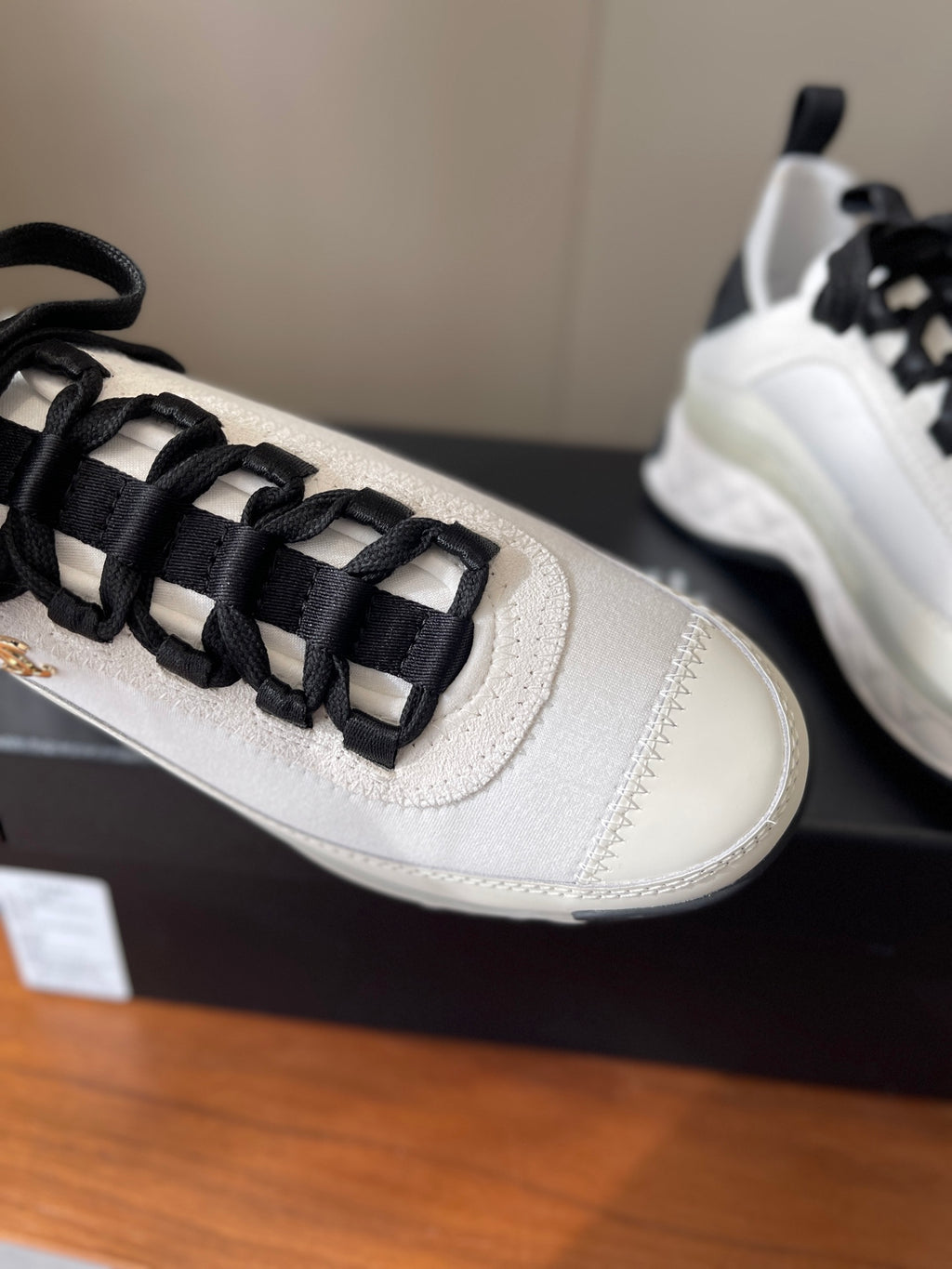 White sneaker toe with black lace cage overlay and small metallic emblem