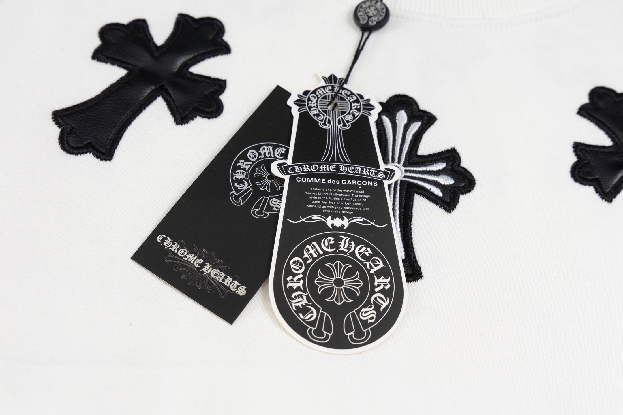 White crewneck sweatshirt detail: black cross pendant graphic and label