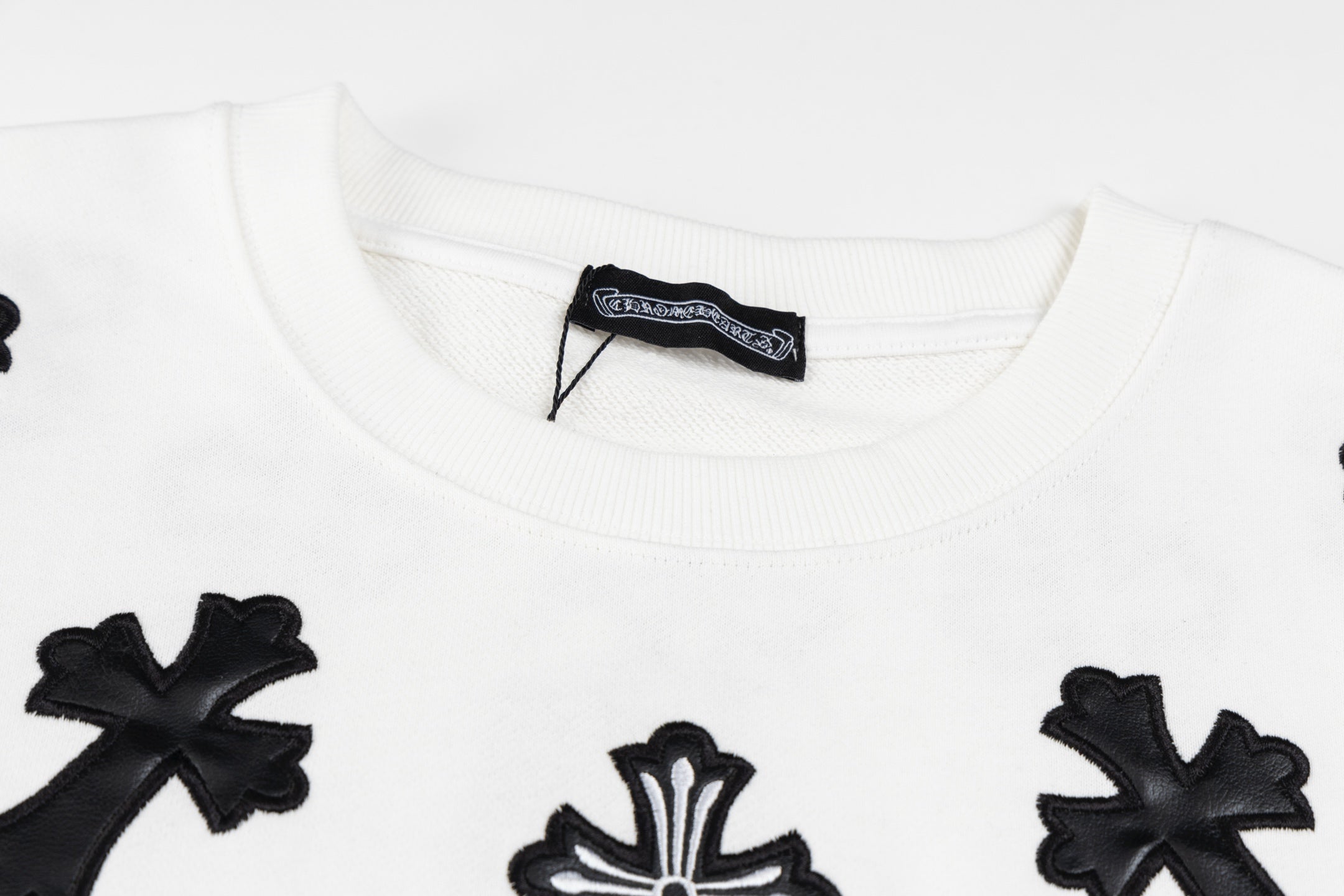 White crewneck sweatshirt neckline with black cross patch and brand label