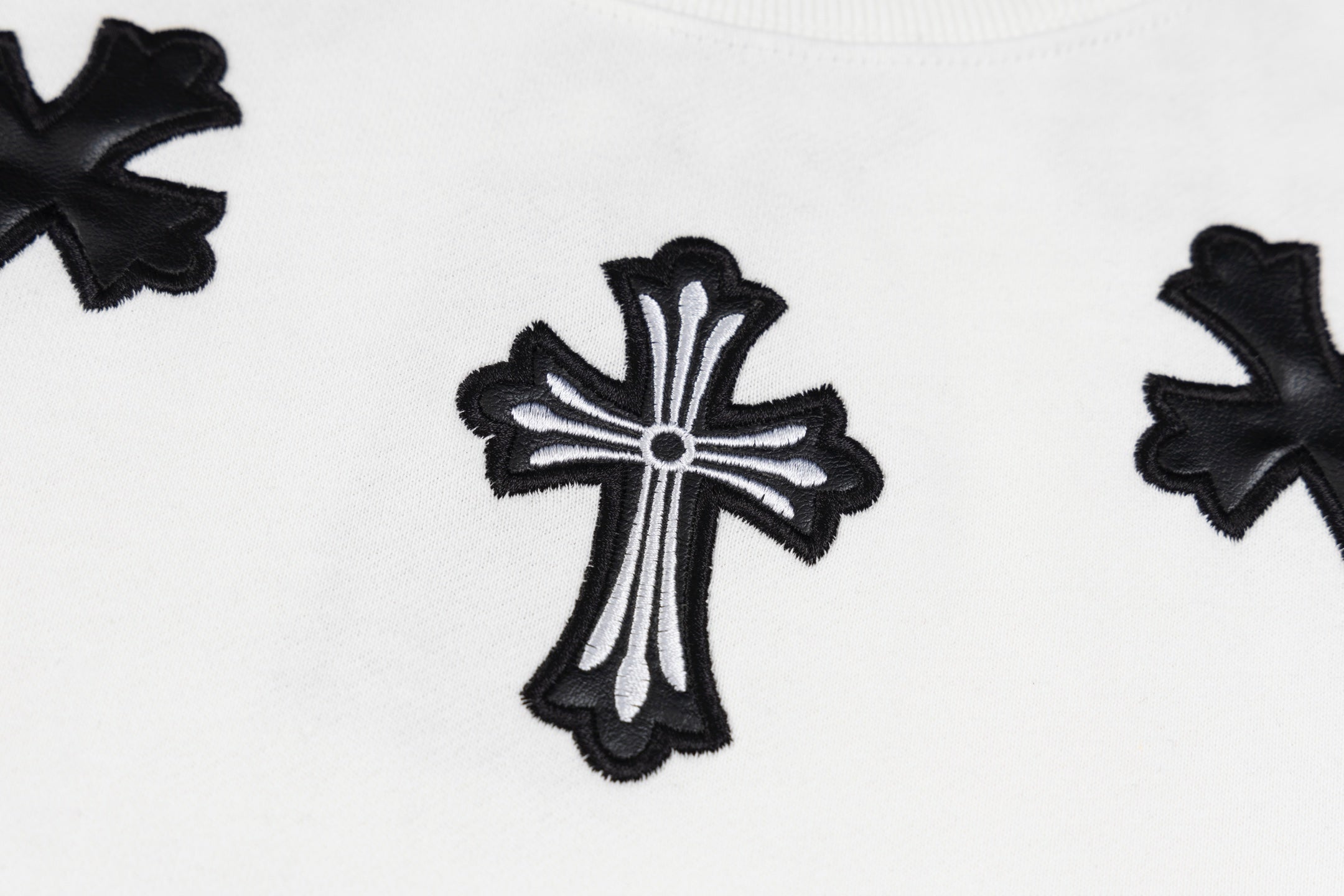 White crewneck sweatshirt with central black cross applique close-up