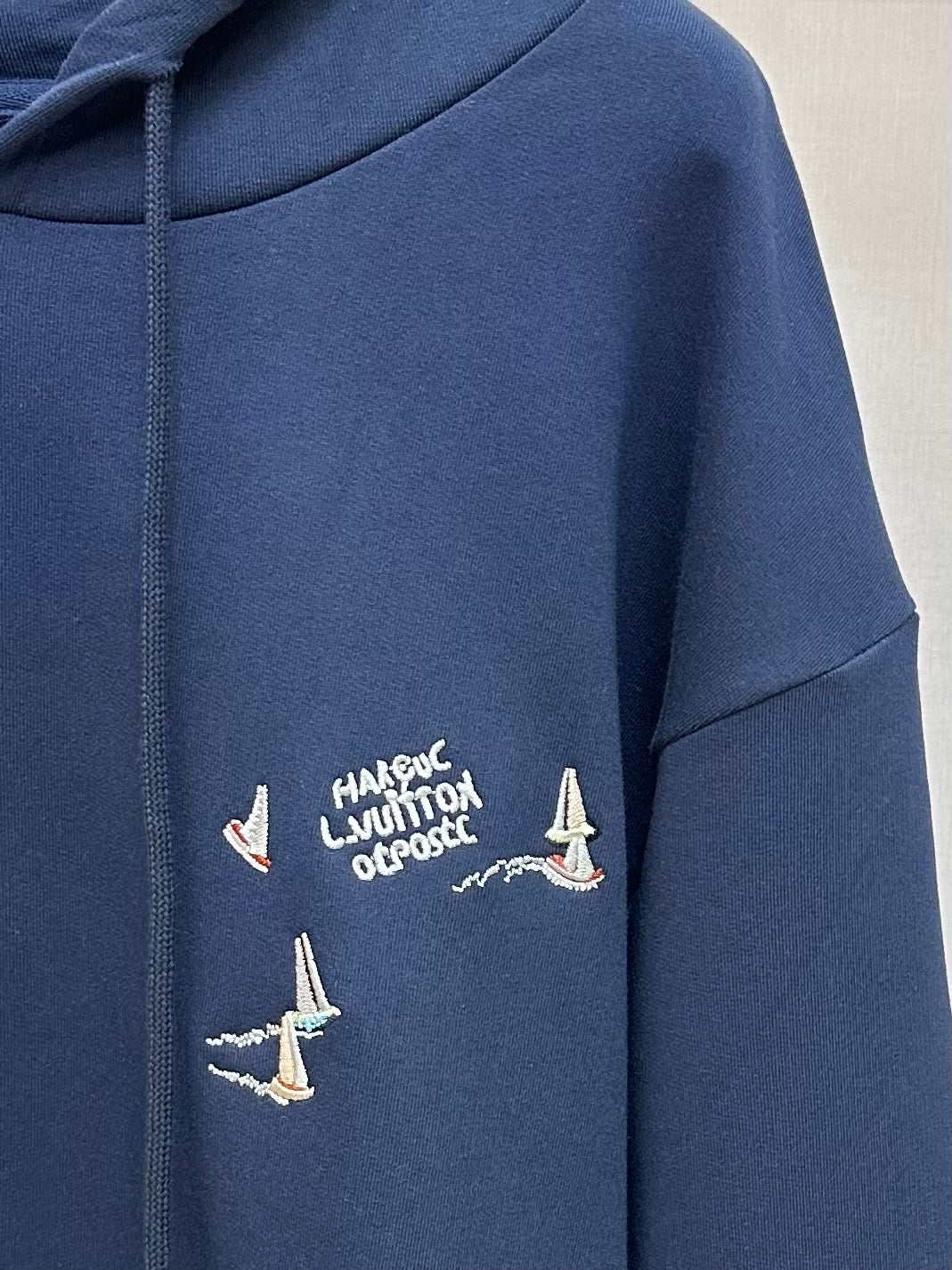 Navy hoodie with graphic text and multiple sailboat prints on chest