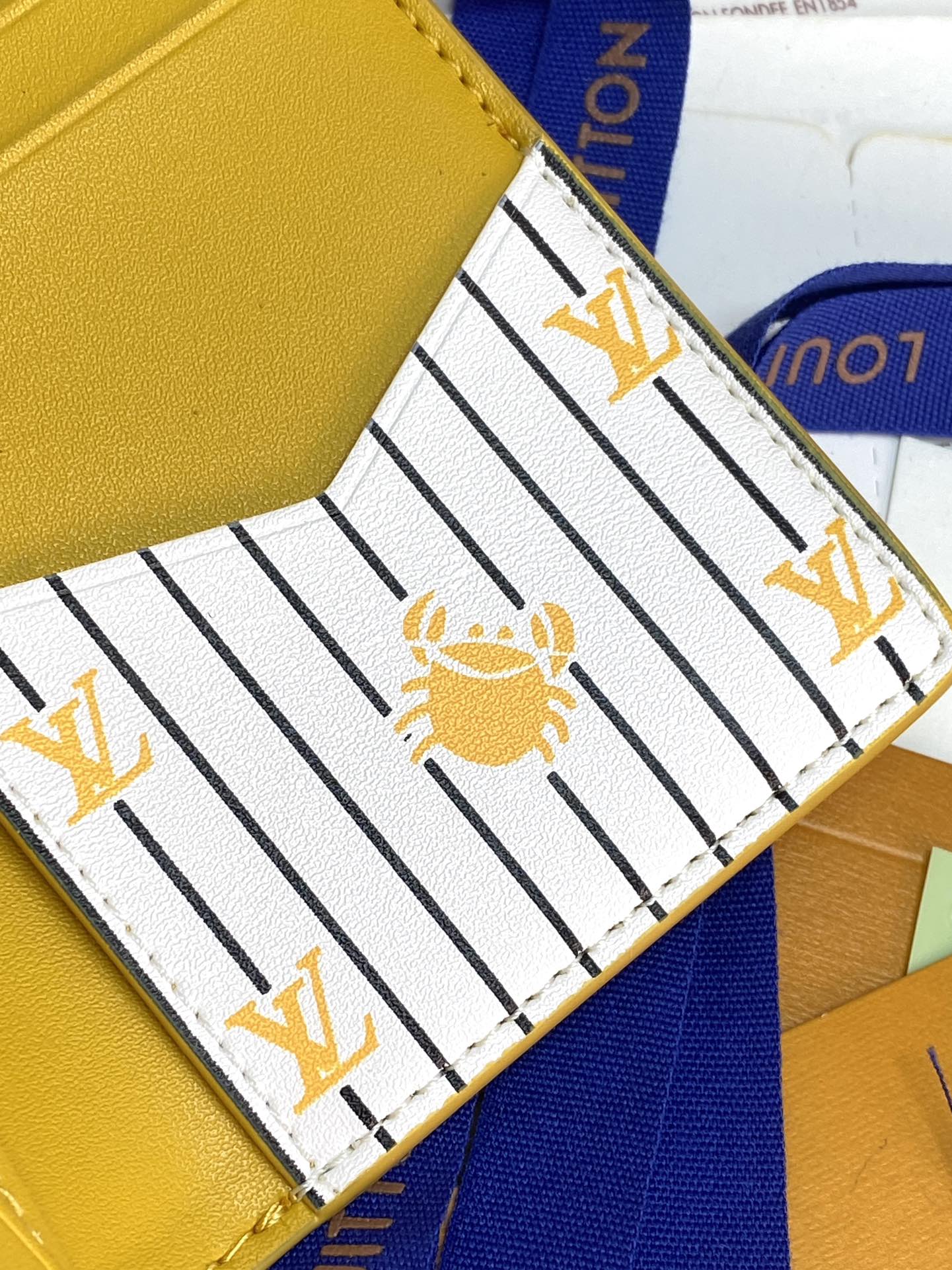 Louis Vuitton card holder interior close-up, striped lining with gold bee motif