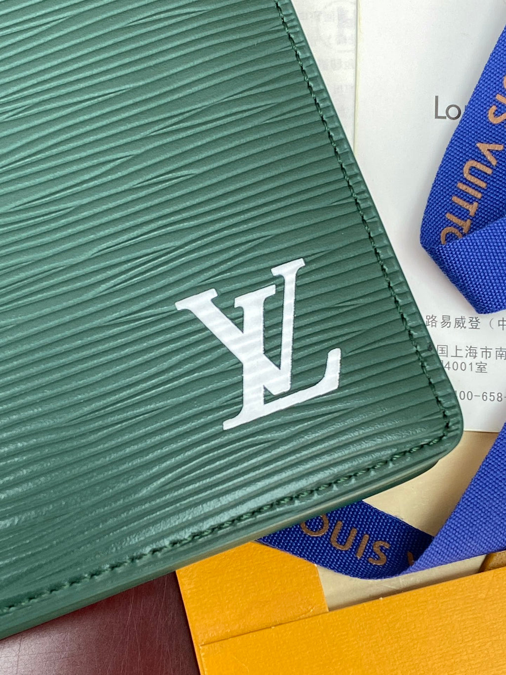 Teal wallet corner with embossed texture and large white LV logo