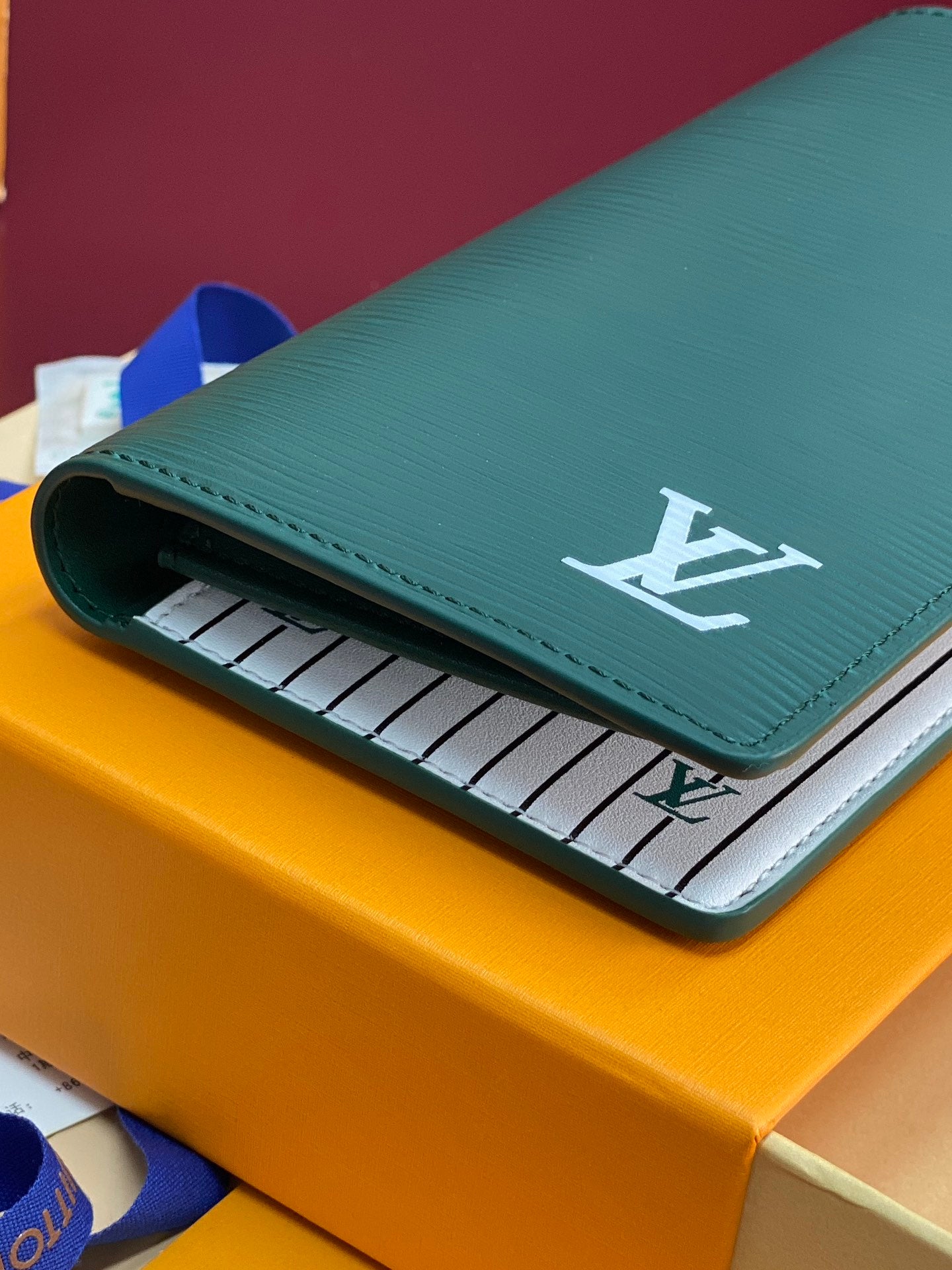 Teal small wallet folded with front flap and white LV logo over striped lining