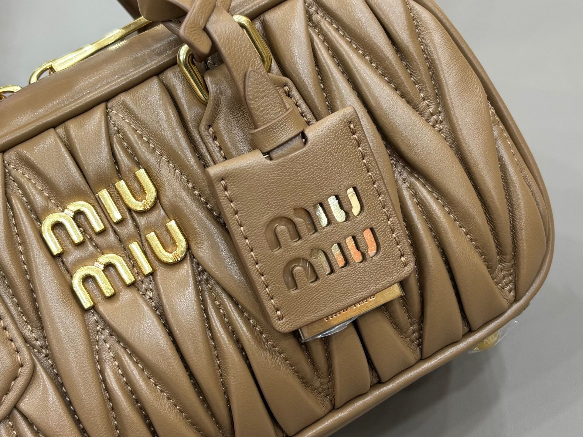 Taupe quilted leather bag detail with two front Miu Miu logo plaques and stitching