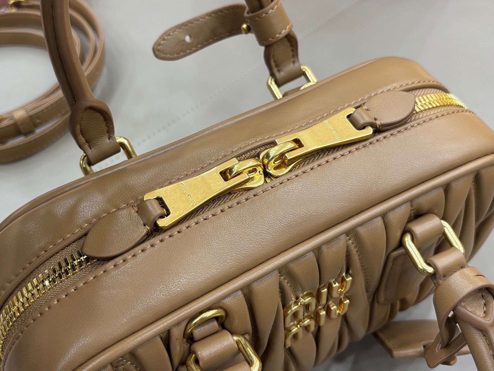 Taupe leather bag strap and gold buckle hardware with front zipper pocket detail
